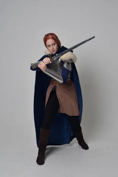 一个红头发的女孩穿着中世纪的战士服装 蓝色天鹅绒斗篷和钢甲 站在灰色的工作室背景的姿势的全长肖像 — 图库照片