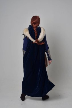 Ortaçağ savaşçı kostüm, mavi kadife pelerin ve çelik zırh, ayakta poz gri studio arka plan üzerinde kırmızı saçlı kız portresi tam uzunlukta.