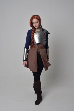 Ortaçağ savaşçı kostüm ve çelik zırh, ayakta poz gri studio arka plan üzerinde kırmızı saçlı kız portresi tam uzunlukta.