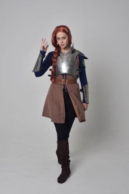 Ortaçağ savaşçı kostüm ve çelik zırh, ayakta poz gri studio arka plan üzerinde kırmızı saçlı kız portresi tam uzunlukta.