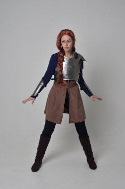 Ortaçağ savaşçı kostüm ve çelik zırh, ayakta poz gri studio arka plan üzerinde kırmızı saçlı kız portresi tam uzunlukta.