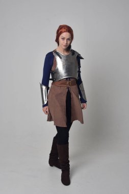 Ortaçağ savaşçı kostüm ve çelik zırh, ayakta poz gri studio arka plan üzerinde kırmızı saçlı kız portresi tam uzunlukta.