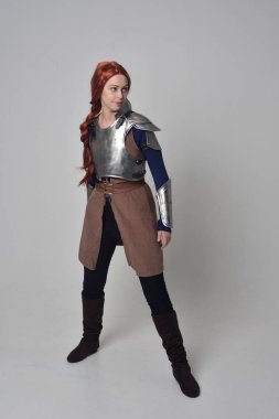 Ortaçağ savaşçı kostüm ve çelik zırh, ayakta poz gri studio arka plan üzerinde kırmızı saçlı kız portresi tam uzunlukta.