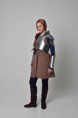 Ortaçağ savaşçı kostüm ve çelik zırh, ayakta poz gri studio arka plan üzerinde kırmızı saçlı kız portresi tam uzunlukta.