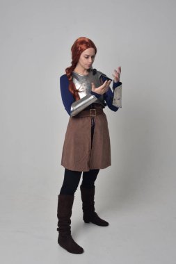 Ortaçağ savaşçı kostüm ve çelik zırh, ayakta poz gri studio arka plan üzerinde kırmızı saçlı kız portresi tam uzunlukta.