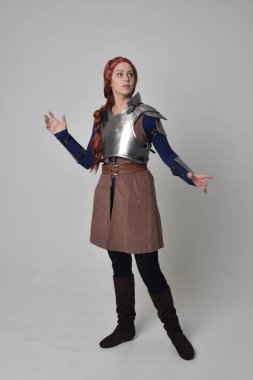 Ortaçağ savaşçı kostüm ve çelik zırh, ayakta poz gri studio arka plan üzerinde kırmızı saçlı kız portresi tam uzunlukta.