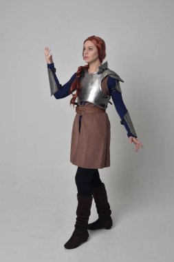 Ortaçağ savaşçı kostüm ve çelik zırh, ayakta poz gri studio arka plan üzerinde kırmızı saçlı kız portresi tam uzunlukta.