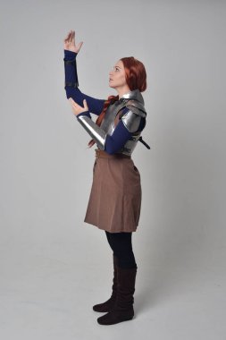 Ortaçağ savaşçı kostüm ve çelik zırh, ayakta poz gri studio arka plan üzerinde kırmızı saçlı kız portresi tam uzunlukta.