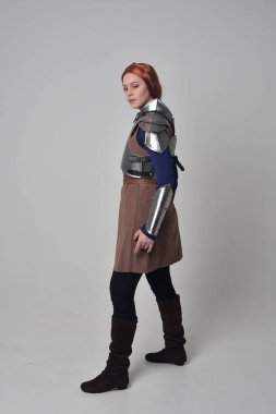 Ortaçağ savaşçı kostüm ve çelik zırh, ayakta poz gri studio arka plan üzerinde kırmızı saçlı kız portresi tam uzunlukta.