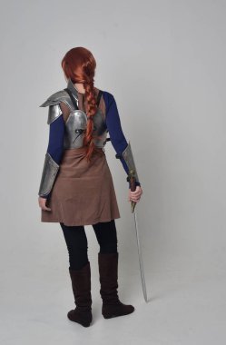 tam uzunlukta bir kılıç tutan Ortaçağ savaşçı kostüm ve çelik zırh giyen bir kırmızı saçlı kız portresi. gri studio arka plan üzerinde ayakta poz.