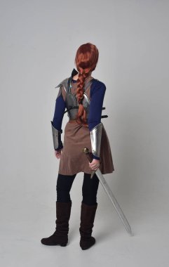 tam uzunlukta bir kılıç tutan Ortaçağ savaşçı kostüm ve çelik zırh giyen bir kırmızı saçlı kız portresi. gri studio arka plan üzerinde ayakta poz.