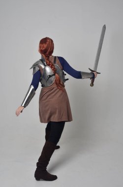 tam uzunlukta bir kılıç tutan Ortaçağ savaşçı kostüm ve çelik zırh giyen bir kırmızı saçlı kız portresi. gri studio arka plan üzerinde ayakta poz.