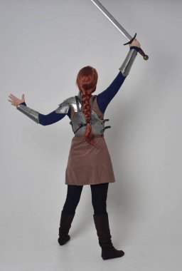 tam uzunlukta bir kılıç tutan Ortaçağ savaşçı kostüm ve çelik zırh giyen bir kırmızı saçlı kız portresi. gri studio arka plan üzerinde ayakta poz.