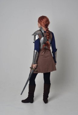 tam uzunlukta bir kılıç tutan Ortaçağ savaşçı kostüm ve çelik zırh giyen bir kırmızı saçlı kız portresi. gri studio arka plan üzerinde ayakta poz.