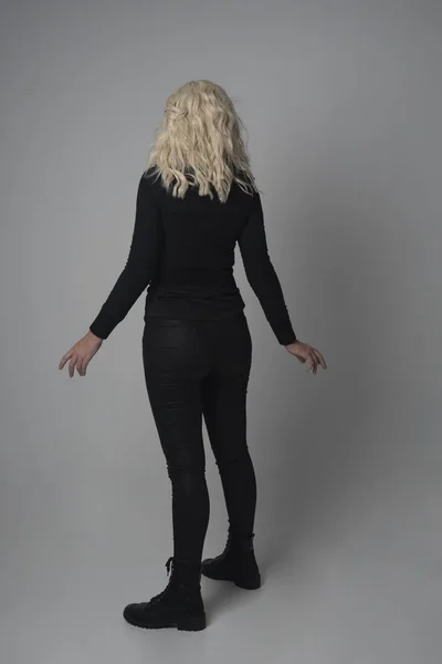 金髪少女をモダンな黒いジャケットとズボンを身に着けている灰色のスタジオの背景に立ちポーズの完全な長さの肖像画 — ストック写真