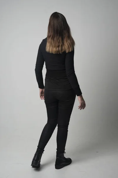 一个穿现代黑色夹克和裤子的黑发女孩的全长肖像 站在灰色工作室背景的镜头前摆姿势 — 图库照片