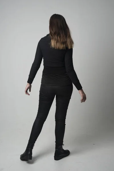 一个穿现代黑色夹克和裤子的黑发女孩的全长肖像 站在灰色工作室背景的镜头前摆姿势 — 图库照片