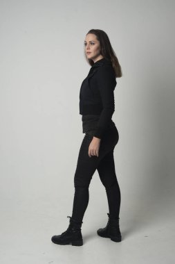 modern siyah ceket ve pantolon giyen bir esmer kız ayakta poz gri studio arka plan üzerinde tam uzunlukta portresi.