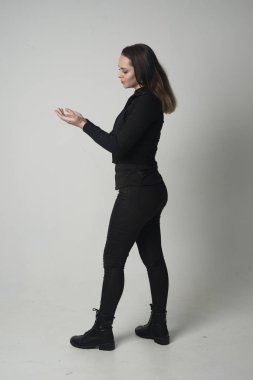 modern siyah ceket ve pantolon giyen bir esmer kız ayakta poz gri studio arka plan üzerinde tam uzunlukta portresi.