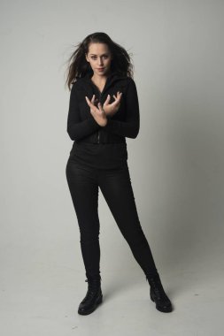 modern siyah ceket ve pantolon giyen bir esmer kız ayakta poz gri studio arka plan üzerinde tam uzunlukta portresi.