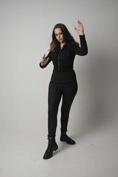 一个穿现代黑色夹克和裤子的黑发女孩的全长肖像 站在灰色的工作室背景摆姿势 — 图库照片
