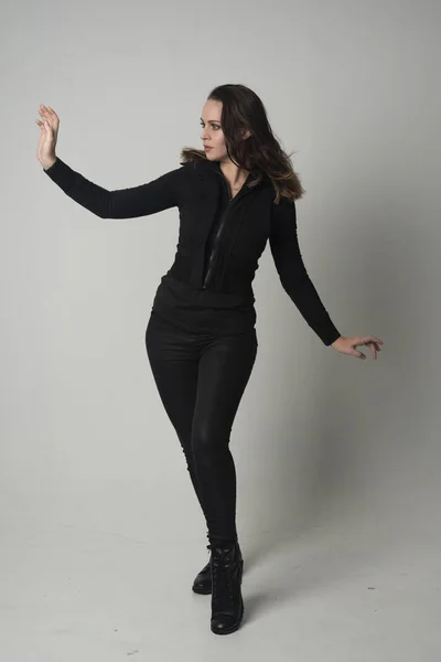 一个穿现代黑色夹克和裤子的黑发女孩的全长肖像 站在灰色的工作室背景摆姿势 — 图库照片