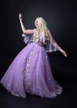 bir fantezi peri ilham kostüm giyen bir sarışın kız tam uzunlukta portre, peri kanatları ile uzun mor balo elbisesi, karanlık bir stüdyo arka planda ayakta poz.