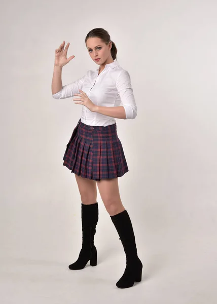 白いシャツとチェック柄のスカートのユニフォームを着たブルネットの女の子のフルレングスの肖像画 クリームスタジオの背景に立ってポーズ — ストック写真