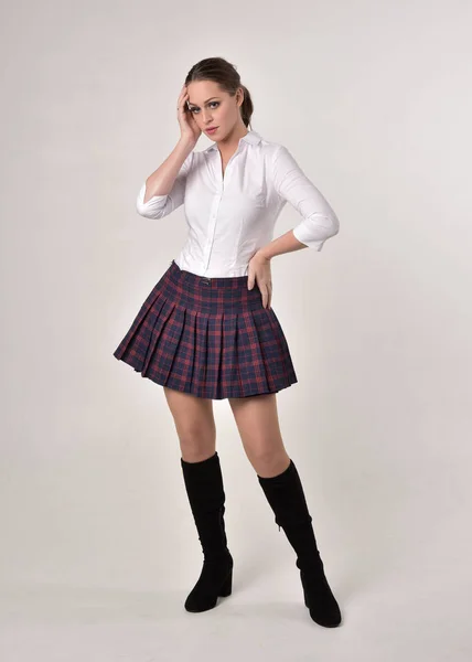 白いシャツとチェック柄のスカートのユニフォームを着たブルネットの女の子のフルレングスの肖像画 クリームスタジオの背景に立ってポーズ — ストック写真