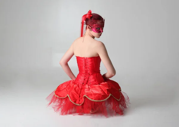 一个穿着红色芭蕾舞衣和面具的女孩的全长肖像 坐在工作室背景上的姿势 — 图库照片