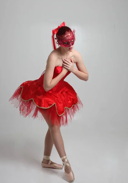 full length portrait of girl wearing red ballerina tutu and mask. dancing pose against a studio background.