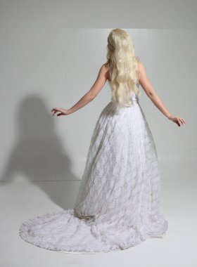 uzun beyaz dantel gelinlik giyen sarışın kız tam uzunlukta portre. bir stüdyo arka plan üzerinde ayakta poz.