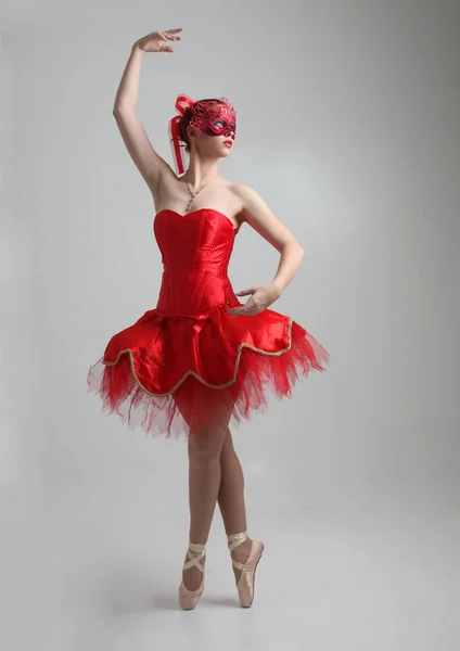 full length portrait of girl wearing red ballerina tutu and mask. dancing pose against a studio background.