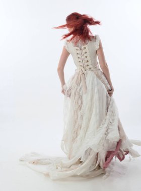 yırtık ve yırtık gelinlik giyen kırmızı saçlı kız tam uzunlukta portre. Beyaz bir stüdyo arka plan karşı Ayakta poz.