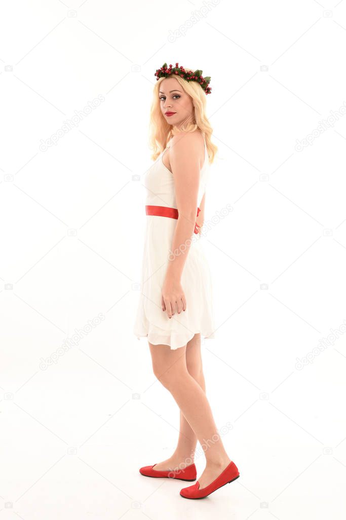 full length portrait of blonde girl wearing a white dress and flower crown.  Standing pose, isolated against a  white studio background.