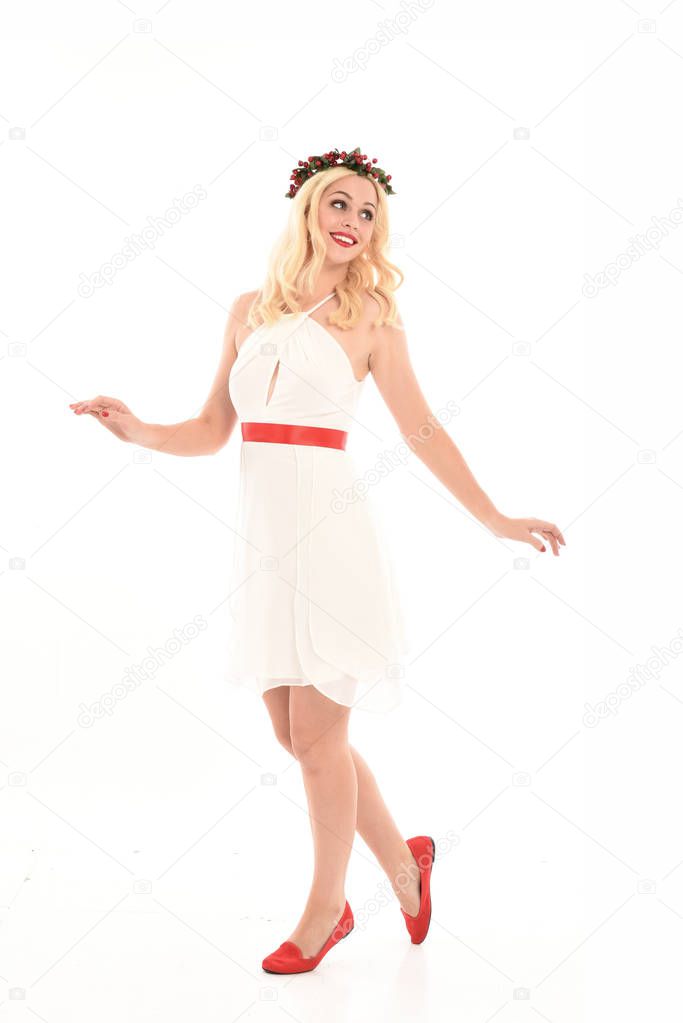 full length portrait of blonde girl wearing a white dress and flower crown.  Standing pose, holding red present,  isolated against a  white studio background.