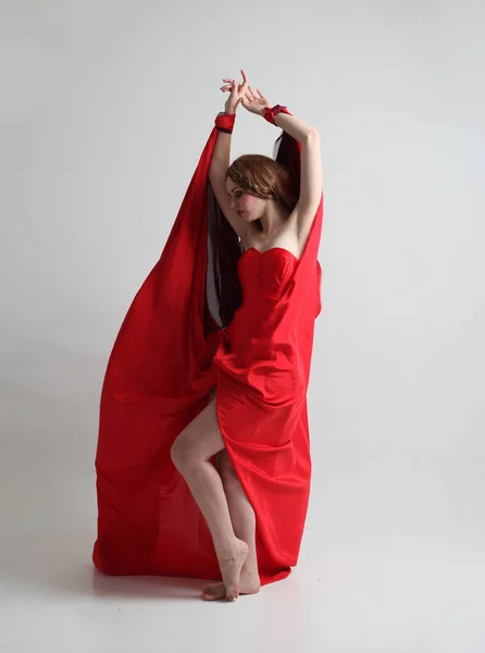 一个穿着红色长丝质长袍的女孩的全长肖像 站在灰色工作室背景的姿势 — 图库照片