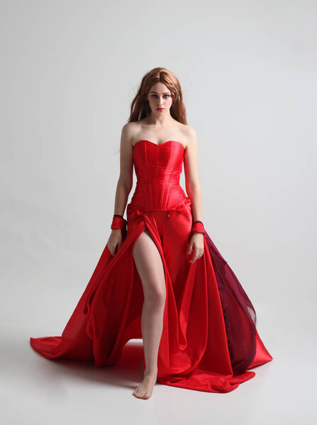 full length portrait of a  girl wearing a long red silk gown, Standing pose on a grey studio background.