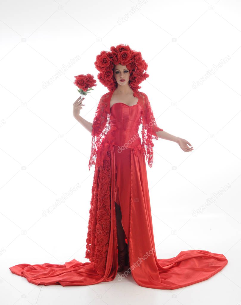 full length portrait of girl wearing long red silk gown and flower headdress. standing pose on white studio background.