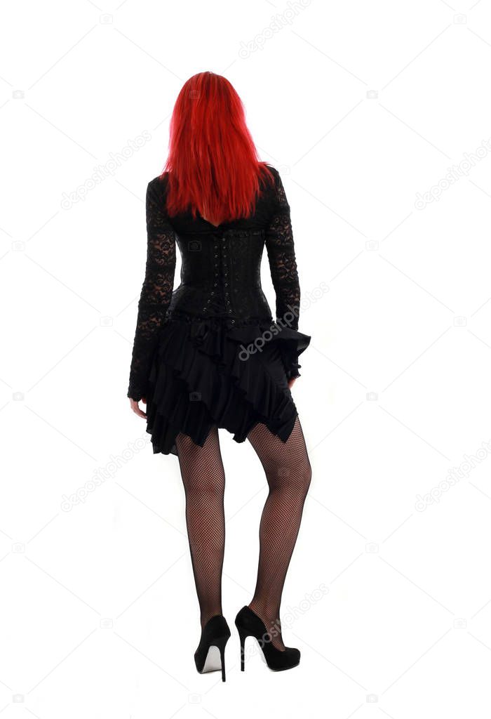 full length portrait of a  red haired girl wearing a  black gothic gown, Standing pose on a grey studio background.