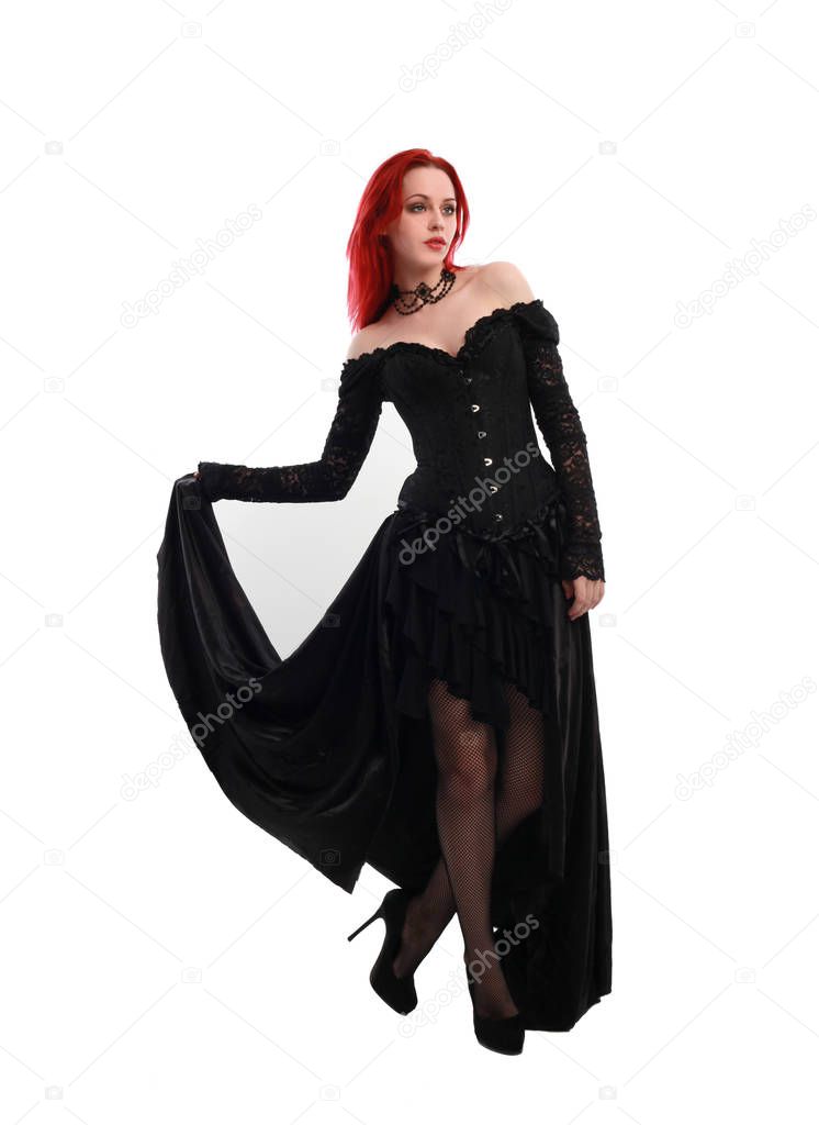 full length portrait of a  red haired girl wearing a  black gothic gown, Standing pose on a grey studio background.