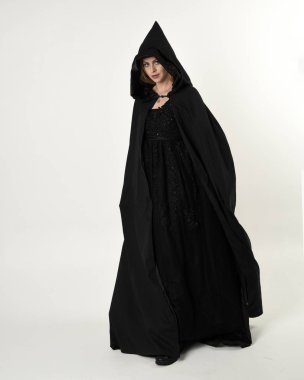 Uzun boylu, siyah pelerinli, beyaz bir stüdyo arka planda duran sarışın bir kızın portresi..