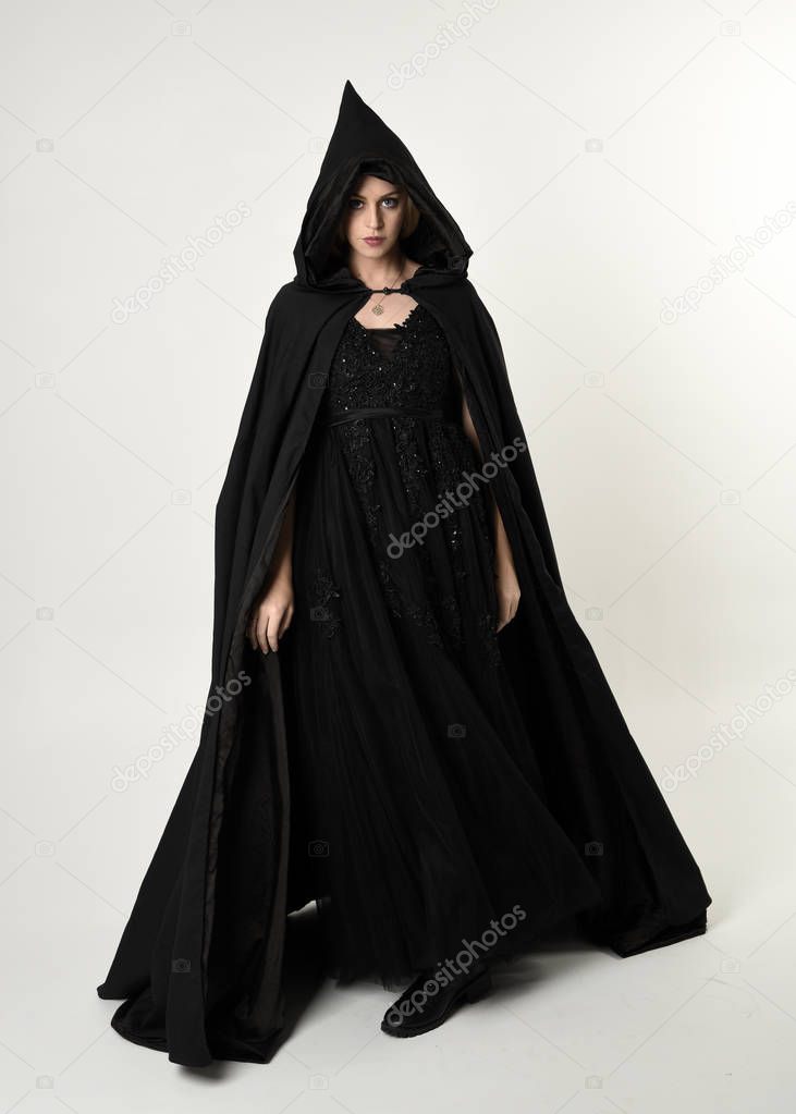 full length portrait of blonde girl wearing long black flowing cloak, standing pose  with  a white studio background.