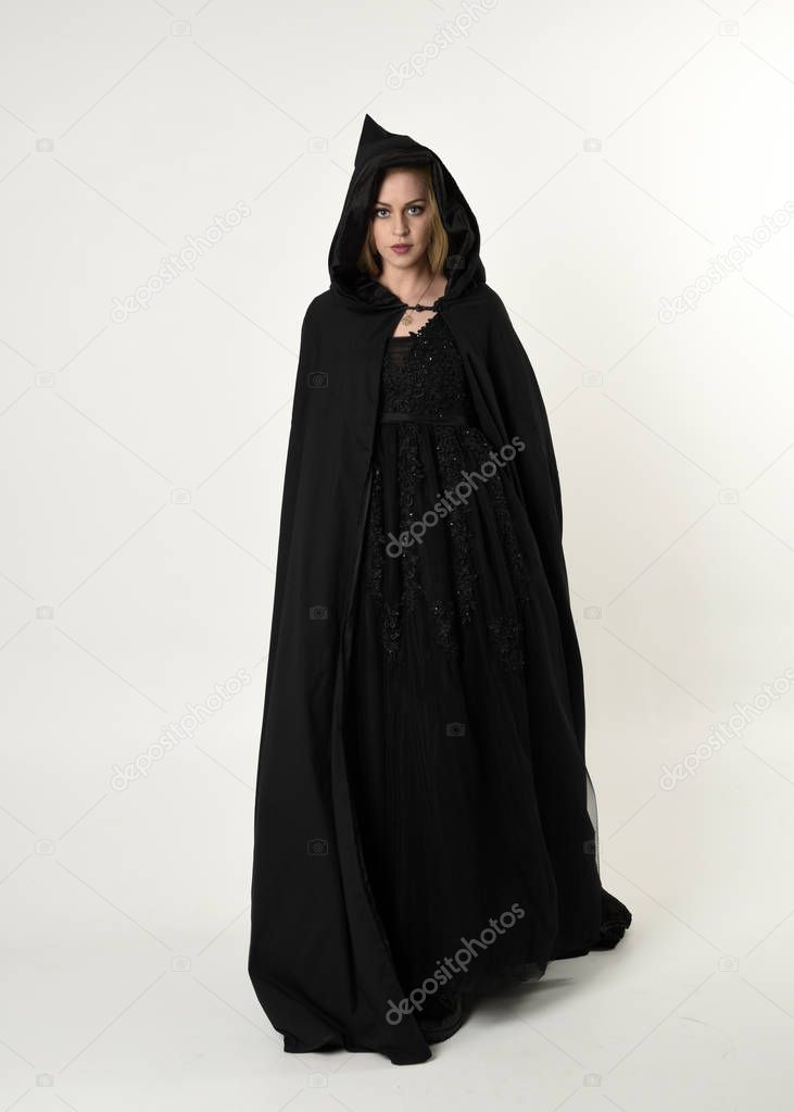 full length portrait of blonde girl wearing long black flowing cloak, standing pose  with  a white studio background.