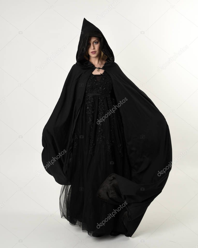 full length portrait of blonde girl wearing long black flowing cloak, standing pose  with  a white studio background.