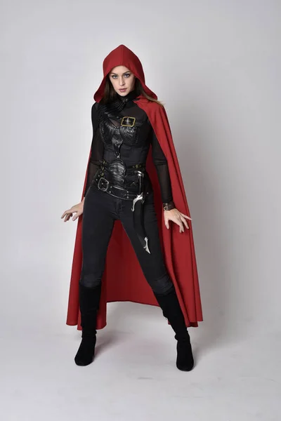 全长肖像一个漂亮的黑发女人穿着黑色皮革幻想服装与长长的红色超级英雄斗篷 站在工作室背景上的姿势 — 图库照片
