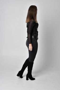 Siyah deri fantezi kostümlü ve hançerli güzel esmer bir kadının tam boy portresi. Stüdyonun arka planında kameradan uzak dur..