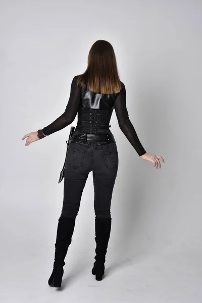 全长肖像一个漂亮的黑发女人穿着黑色皮革幻想服装与匕首 面对镜头站在摄影棚前的姿势 — 图库照片