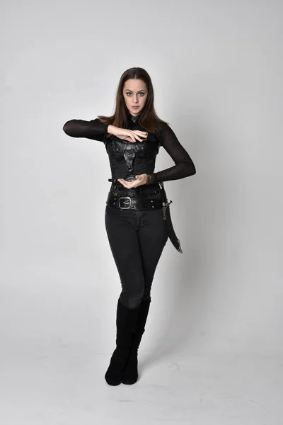 全长肖像一个漂亮的黑发女人穿着黑色皮革幻想服装与匕首 站在工作室背景上的姿势 — 图库照片