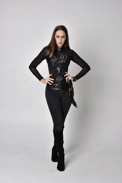 全长肖像一个漂亮的黑发女人穿着黑色皮革幻想服装与匕首 站在工作室背景上的姿势 — 图库照片
